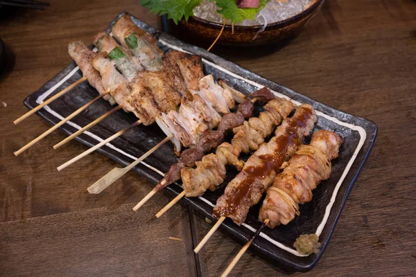 焼き鳥と呼ばれる鶏肉の串焼きは 居酒屋で人気の日本料理です 暗い茶色の木製のテーブルの上に — ストック写真