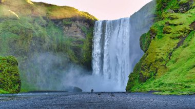 Güney İzlanda 'da yaz mevsimi boyunca Skogafoss Şelalesi' nde iki turist duruyor..