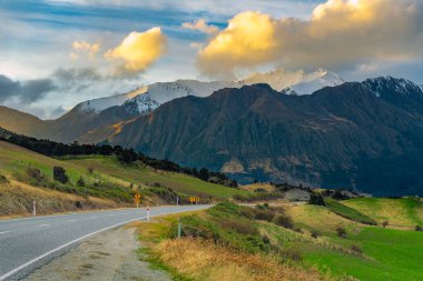 Wanaka Otago, Newzealand 'da güneş battığında dağ ve yol manzarası. Güzel sarı bir bulut vardı..