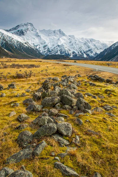 Tepesinde kar olan yüksek dağlar ve kışın otobanlar. Yol kenarındaki çimenler Yeni Zelanda, Yeni Zelanda 'daki Ulusal Park bölgesinde sarı renktedir.