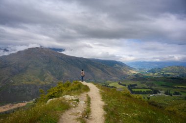 Bir adam, Yeni Zelanda, Otago 'da yaz boyunca Arrow kavşağında panoramik bir manzara görmek için bir tepede duruyor..