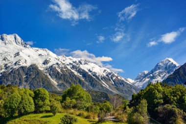 Dağın tepesindeki yüksek dağ manzaraları yaz aylarında gökyüzünde beyaz kar ve Yeni Zelanda 'nın güneyindeki Mount Cook Ulusal Parkı' nda yeşil çimlerle kaplı bulutlardır..
