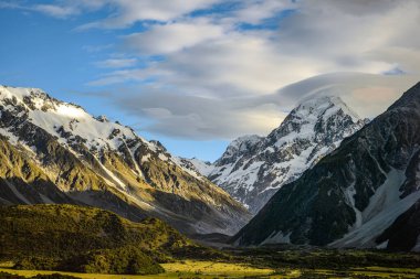 Dağın tepesindeki yüksek dağ manzaraları yaz aylarında gökyüzünde beyaz kar ve Yeni Zelanda 'nın güneyindeki Mount Cook Ulusal Parkı' nda yeşil çimlerle kaplı bulutlardır.