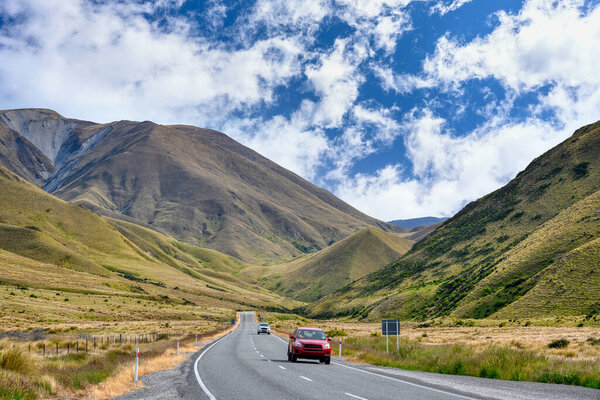 A red car ran on a highway in the valley at the Lindis Pass Summit scenic look out in summer season in Otago, New Zealand.