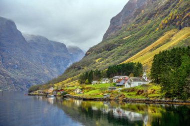 Rıhtımdaki küçük bir köy ve sonbahar mevsiminde suyu yansıtan dağlar. Gudvangen 'den Norveç' teki Flam 'e kadar olan Sognefjord Cruise' un güzelliğini görmek için bir tekne gezisinden izleyin..