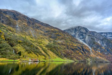 Rıhtımdaki küçük bir köy ve sonbahar mevsiminde suyu yansıtan dağlar. Gudvangen 'den Norveç' teki Flam 'e kadar olan Sognefjord Cruise' un güzelliğini görmek için bir tekne gezisinden izleyin..