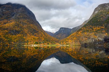 Rıhtımdaki küçük bir köy ve sonbahar mevsiminde suyu yansıtan dağlar. Gudvangen 'den Norveç' teki Flam 'e kadar olan Sognefjord Cruise' un güzelliğini görmek için bir tekne gezisinden izleyin..