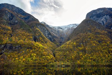 Sonbahar mevsiminde fiyort ve dağlar suyu yansıtır. Gudvangen 'den Norveç' teki Flam 'e kadar olan Sognefjord Cruise' un güzelliğini görmek için bir tekne gezisinden izleyin..