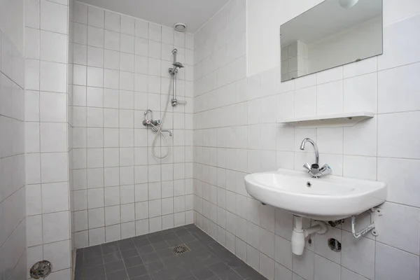 Simple, old clean bathroom with white tiled floor sink and shower Royalty Free Stock Images