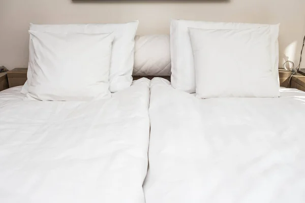 Bed maid-up with clean white pillows and bed sheets in beauty room. Close-up. Lens flair in sunlight.