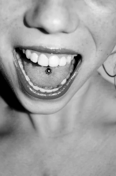 Beautiful woman sticking out her tongue and showing her young piercing black and white — Stock Photo, Image