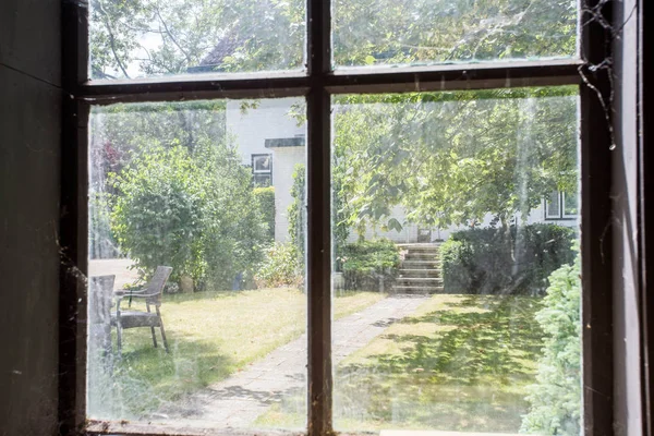 View from an abandoned building with a dirty old window looking at overrun cozy green garden Royalty Free Stock Photos