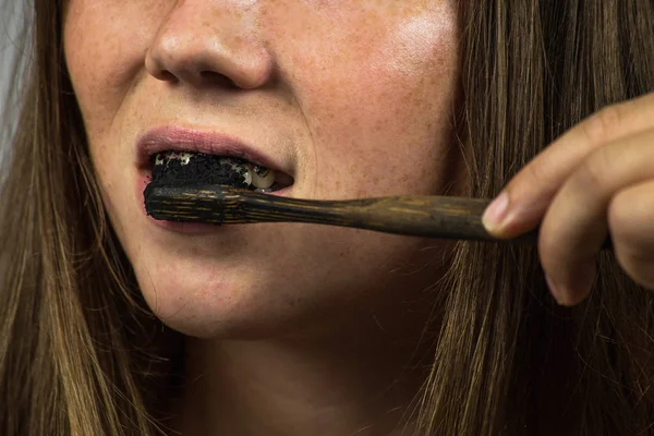 Young woman brushing her teeth with a black tooth paste with active charcoal, and black tooth brush on white background for Teeth whitening — Stock Photo, Image