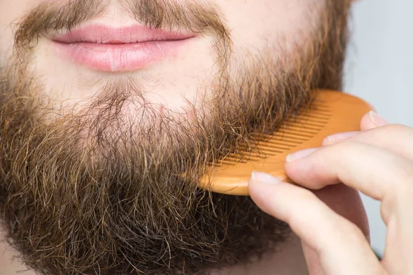 Closeup Mladého Muže Styling Dlouhé Vousy Hřebenem Stoje Sama Studiu — Stock fotografie