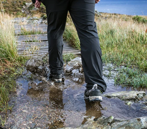 Vandringsskor på vandrare i vattenpöl i rmountain landskap. Mannen vandrare vandring stövlar i närbild. Manliga fötter. — Stockfoto