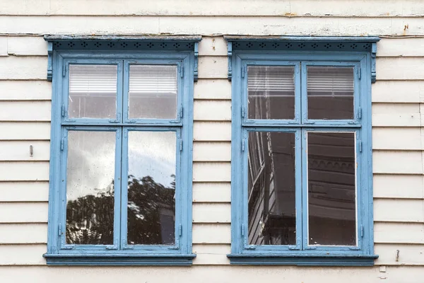 Two blue windows side by side on a rough and uneven wooden wall. abstract close-up