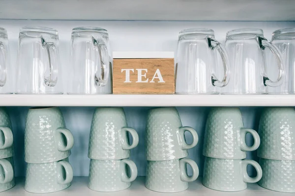 Xícaras de chá e canecas de café em uma prateleira de cozinha com uma caixa de chá foco Rack. Fechar . — Fotografia de Stock