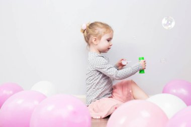 Sarışın güzel kız vardır mutlu eğlenceli neşeli gülümseyen yüzü, pembe elbise, sabun köpüğü üfleyici. Pembe ve beyaz balonları mutlu portre