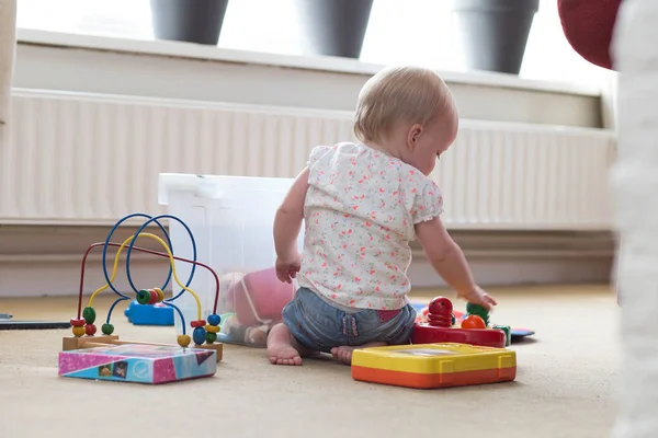 Bebê brincando sozinho com brinquedos em um tapete no chão em casa — Fotografia de Stock