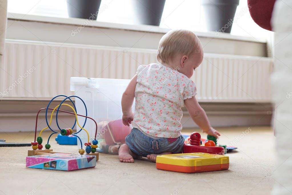 Baby playing alone with toys on a carpet on the floor at home