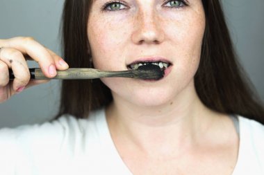 Genç kadın bir siyah diş hamur aktif kömür ile dişlerini fırçalama ve beyazlatma dişler için beyaz arka planda siyah diş fırçası