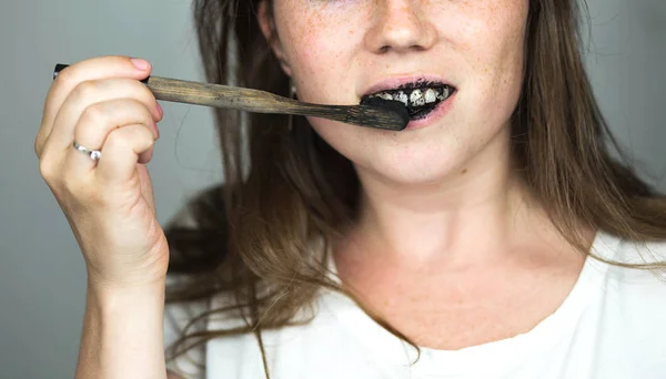 Young woman brushing her teeth with a black tooth paste with active charcoal, and black tooth brush on white background for Teeth whitening — Stock Photo, Image