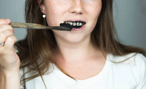 Młoda kobieta szczotkowanie zębów pastą czarny zęba z węglem aktywnym, i szczoteczka do zębów czarno na białym tle dla zębów Wybielanie — Zdjęcie stockowe
