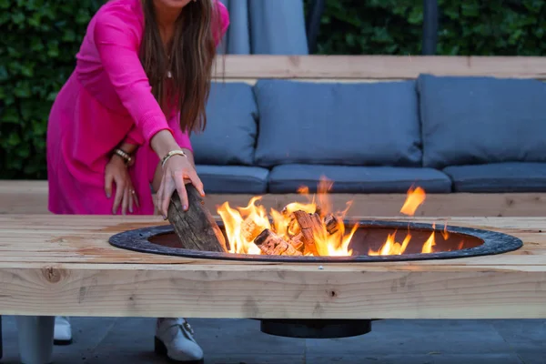 Frau wirft an einem Sommertag Baumstämme auf Feuerstelle im Garten — Stockfoto
