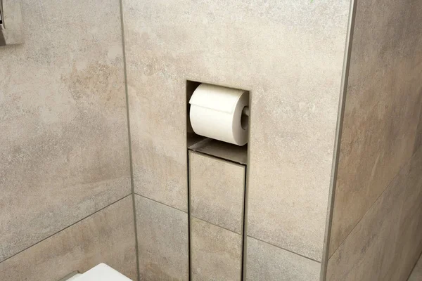 Un rotolo bianco di carta igienica morbida ordinatamente appeso a un moderno supporto cromato nel muro — Foto Stock