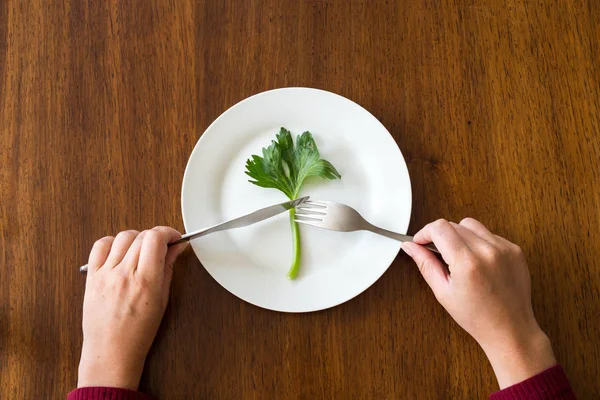 Έννοια της διατροφής. ένα πράσινο λαχανικό σε άδειο λευκό πιάτο με γυναικεία χέρια, σέλινο σε ξύλινο τραπέζι υγιεινό — Φωτογραφία Αρχείου