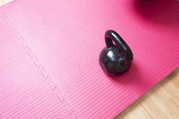 Kettlebell and pink yoga mat on the floor, sport concept space for text