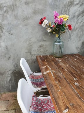 Ahşap bir masada vazoda renkli çiçeklerle beton duvar, modern odada dekorasyon.