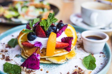Çeşitli meyve, ejderha meyve ve yaban mersini ve şurubu ile krep yığını