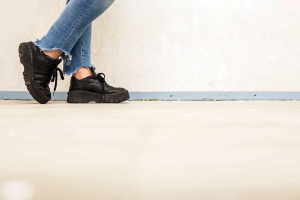 Wanita dengan sepatu putih kulit mengenakan jeans biru dan sepatu olahraga berjalan di dekat dinding putih Konsep fashion — Stok Foto