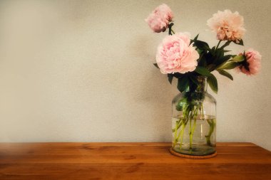 Ahşap masadaki cam vazodaki pembe şakayıklar, modern yazılar için alanı olan romantik tasarım.