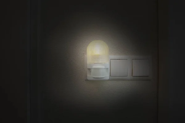 Βύσμα νυχτερινού φωτός σε λευκή υποδοχή στον λευκό τοίχο ενεργοποιείται αυτόματα στο σύγχρονο σπίτι τη νύχτα στο σκοτάδι — Φωτογραφία Αρχείου