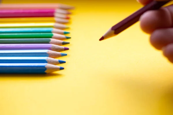 Χρωματιστά μολύβια σε μια σειρά σε χρώματα ουράνιο τόξο, χέρι με μπλε χρώμα μολύβι αντλεί σε πορτοκαλί χαρτί, ρετρό φόντο — Φωτογραφία Αρχείου