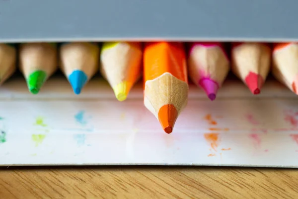 Χρωματιστά μολύβια σε ένα χαρτοκιβώτιο γκρι κουτί, χρώματα ουράνιο τόξο, πορτοκαλί μολύβι ξεχωρίζει μακροεντολή, σχολείο ή γραφείο προμήθειες — Φωτογραφία Αρχείου