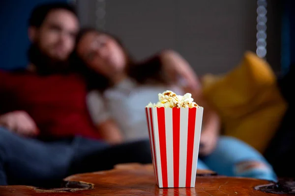 Una joven pareja enamorada viendo la televisión por la noche romántica noche de citas tumbada en el sofá comiendo palomitas de maíz —  Fotos de Stock