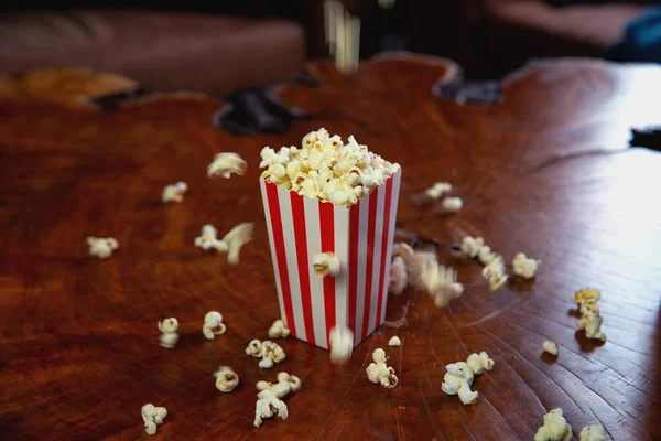 Popcorn terbang keluar dari kotak kardus. ember bergaris-garis merah dan putih dengan popcorn terbang di ruang tamu, film atau konsep bioskop — Stok Foto