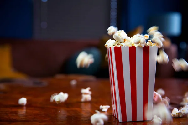 Popcorn terbang keluar dari kotak kardus. ember bergaris-garis merah dan putih dengan popcorn terbang di ruang tamu, film atau konsep bioskop — Stok Foto