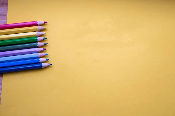 Colored pencils in Rainbow colors in a row on orange background, retro modern design space for text top view
