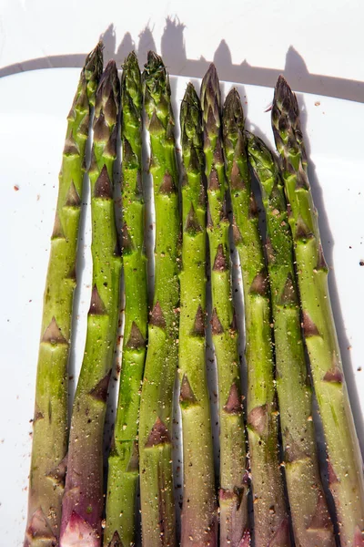 closeup of some raw green asparagus on a white plate, white background top view