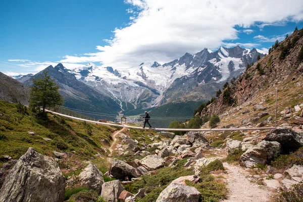 Uma pessoa jovem caminhando em uma ponte suspensa na Suíça, caminhando com uma bela paisagem — Fotografia de Stock