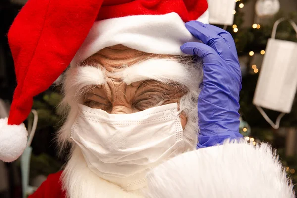 Weihnachtsmann mit Gesichtsmaske und Schutzhandschuhen für Covid-19, Weihnachtsmann am Weihnachtsbaum unglücklich über Coronavirus. — Stockfoto