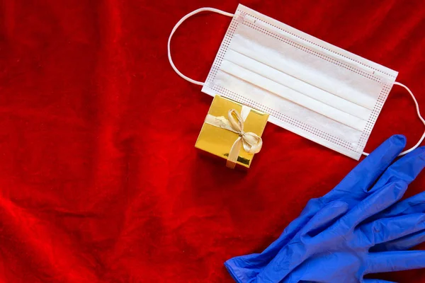 Red Christmas berwarna latar belakang dengan kotak hadiah emas dan topeng medis dan sarung tangan pelindung untuk coronavirus, Covid-19 dan konsep Natal, — Stok Foto