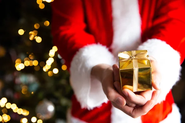 Чоловік у Санта Клаусі костюм біля різдвяної ялинки з золотою коробкою з подарунками на Різдво. — стокове фото