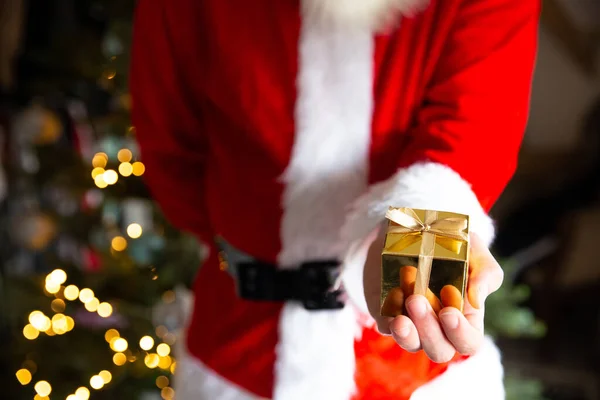 Mann im Weihnachtsmannkostüm in der Nähe des Weihnachtsbaums mit goldener Geschenkschachtel, Weihnachtsgeschenk Hintergrund mit Bokeh-Lichtern — Stockfoto