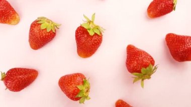 Pastel pembe yüzeyinde dönen kırmızı taze çilek.