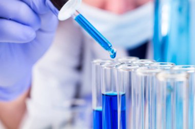 Bilim adamı pipet ve test tüpleri ve mavi sıvı su damlası ile düşmek.